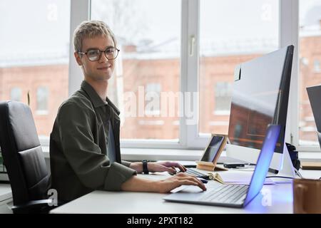 Portrait of young programmer in eyeglasses looking at camera while developing software on computer at his workplace Stock Photo