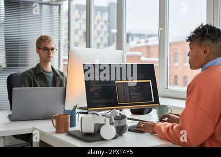 Young colleagues working with security computer codes sitting at table in IT office Stock Photo