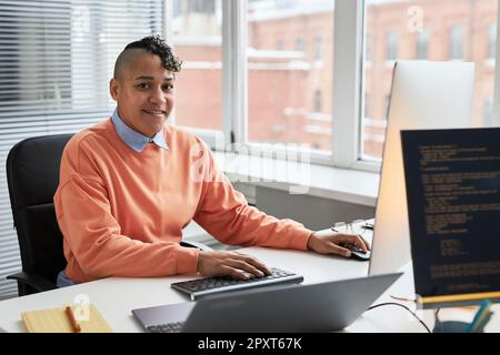 Portrait of young programmer smiling at camera while working with security codes on computer sitting at his workplace Stock Photo