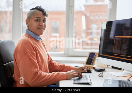 Portrait of professional programmer smiling at camera while writing codes on computer sitting at his workplace Stock Photo