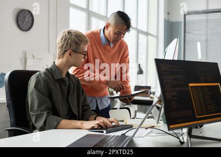 Young man showing presentation on digital tablet to his colleague and discussing development of software with him Stock Photo