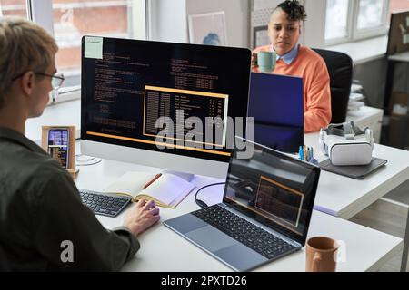 Young programmers writing codes for computer program on computers sitting at workplace in office Stock Photo