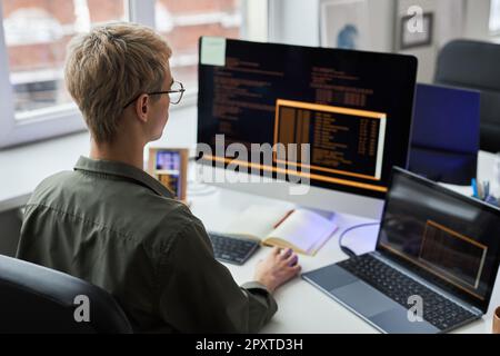 Rear view of young programmer working on computer with codes sitting at his workplace in office Stock Photo