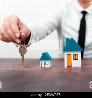 Businesswoman holding keys. olored paper houses standing on desk. Stock Photo
