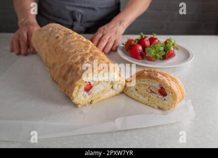Fresh baked and filled swiss roll with whipped cream and strawberry filling on kitchen counter without topping Stock Photo