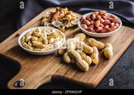 Unpeeled and peeled peanuts in bowl on the kitchen table. Stock Photo