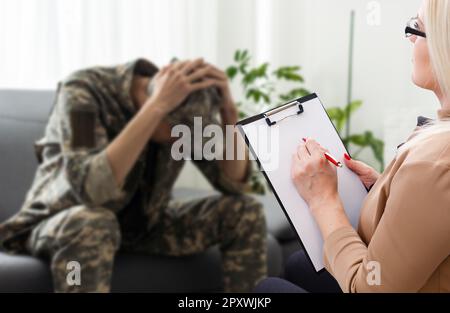 Psychologist making notes during therapy session with sad male soldier, PTSD Stock Photo