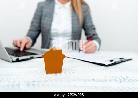 Businesswoman sitting at table writing in notebook and typing on laptop. Stock Photo