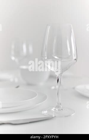 Close up view of empty wine glass on table prepared for dinner with tablecloth and plates, no people. Eating, life event celebration Stock Photo