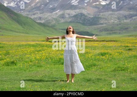 Front view portrait of a happy woman screaming outstretching arms in nature with white dress Stock Photo