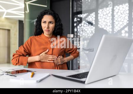 Anxious and scared business woman working inside office, Hispanic woman panic attack and breathing problem, female worker with laptop working. Stock Photo