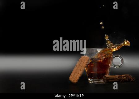 Splash in glass cup of black tea isolated on black background with delicious cookies, copy space detox healthy medicine herb Stock Photo