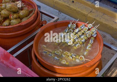 Close-up of a ceramic jar filled with skewers of olives and marinated sardines or anchovies next to another jar filled with aubergines stuffed with al Stock Photo