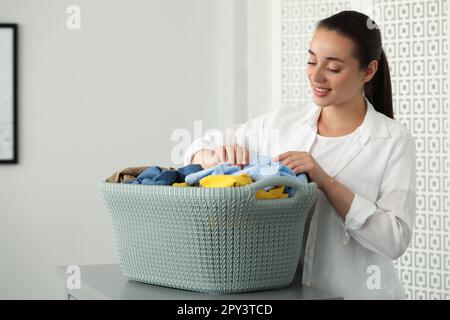 https://l450v.alamy.com/450v/2py3tcd/young-woman-with-basket-full-of-clean-laundry-at-table-indoors-2py3tcd.jpg