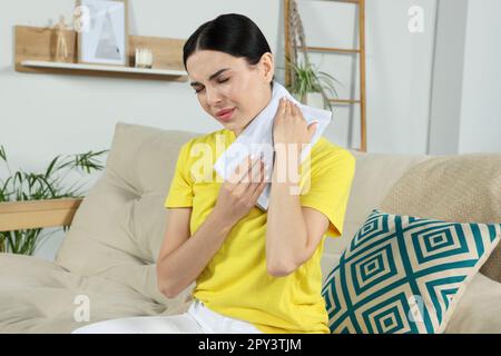 Young woman using heating pad on neck at home Stock Photo