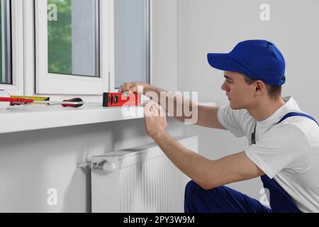 Worker using bubble level after plastic window installation indoors Stock Photo