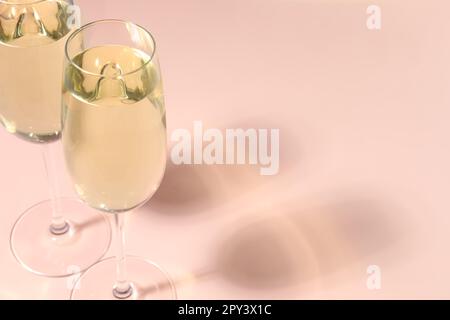 Glasses of delicious sparkling wine on pale pink background, closeup. Space for text Stock Photo