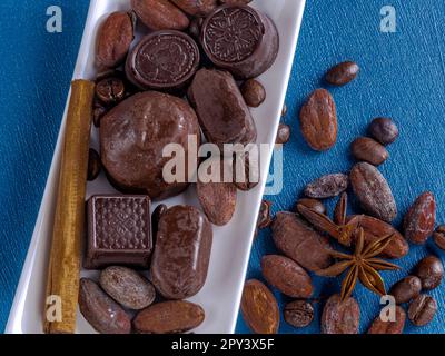 Chocolates in white rectangular tray, accompanied by cocoa beans, coffee and spices. Stock Photo