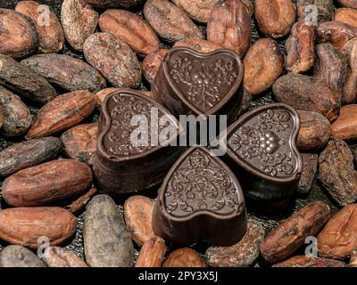 Four chocolates in the shape of a heart on a background of roasted cocoa beans. Stock Photo