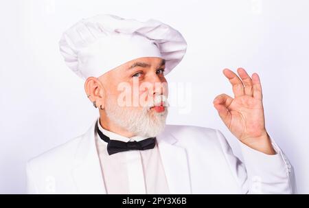 Chef man in white uniform showing sign ok. Bearded cook in chef hat with gesture for approving restaurant service. Professional chef showing sign for Stock Photo