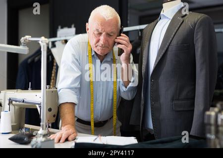 Professional tailor communicates with the client on mobile phone and takes notes in notebook Stock Photo