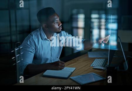 Having goals gives you focus. a young businessman writing in a notebook and using a computer during a late night at work. Stock Photo