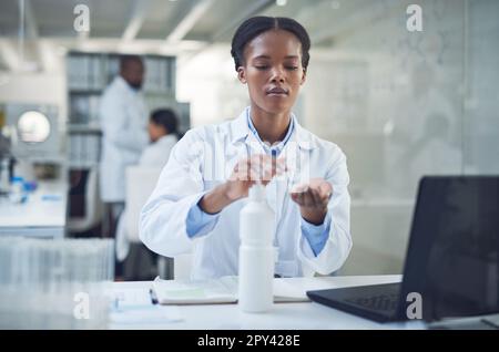 The only bacteria I want is under the microscope. a scientist disinfecting her hands while conducting research in a laboratory. Stock Photo
