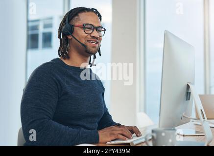 Logging calls and making big sales. a young businessman wearing a headset while working on a computer in an office. Stock Photo
