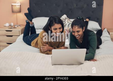 We love the same shows. two young women using a laptop while lying together on a bed. Stock Photo