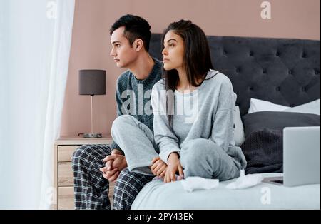 Coupled up in quarantine. a young couple looking thoughtful while recovering from an illness in bed at home. Stock Photo
