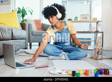 Youd be surprised by how helpful online classes are. a young woman using her laptop while sitting at home with paint and a blank canvas. Stock Photo