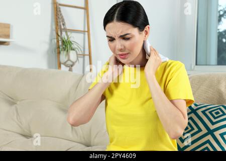 Young woman using heating pad on neck at home Stock Photo