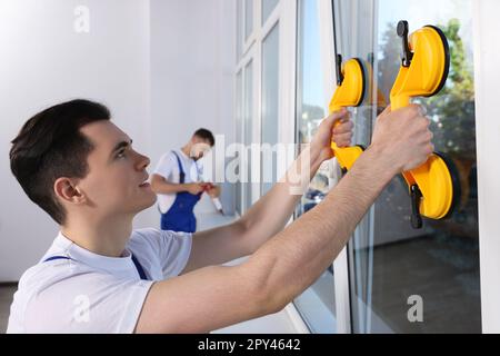 Worker using suction lifters during plastic window installation indoors Stock Photo
