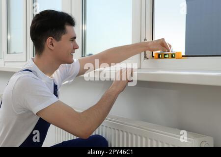 Worker using bubble level after plastic window installation indoors Stock Photo