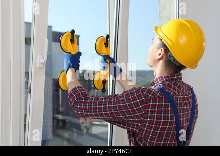 Worker using suction lifters during plastic window installation indoors Stock Photo