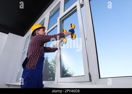 Worker using suction lifters during plastic window installation indoors Stock Photo
