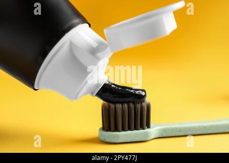 Applying charcoal toothpaste on brush against yellow background, closeup Stock Photo