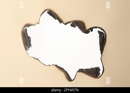 Burnt hole in beige paper on white background Stock Photo