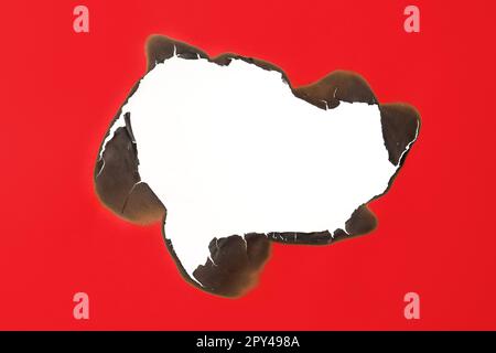 Burnt hole in red paper on white background, space for text Stock Photo