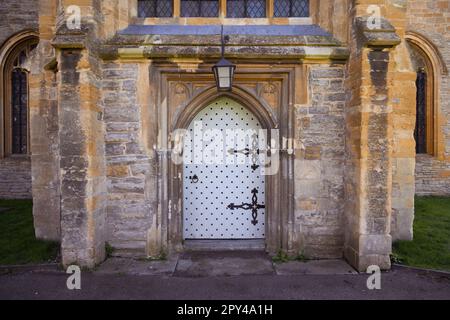 A sturdy, white painted, wooden paneled door with large ornate metal hinges set within an arched stone doorway. Stock Photo