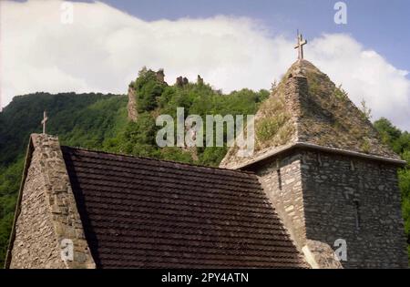 Hunedoara County, Romania, approx. 1999. Exterior view of the 14th century church of the Colt Monastery. In the back, the ruins of the13th century citadel are seen atop the mountain. Stock Photo