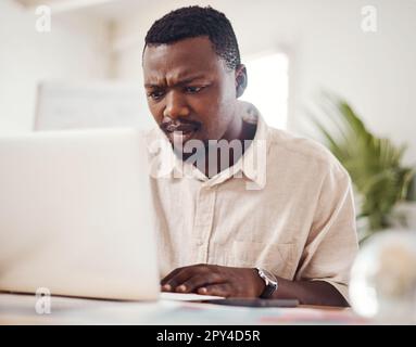 What is happening now...a young businessman looking confused while using a laptop in an office. Stock Photo