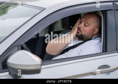 Tired overweight man drives car with broken air conditioner in hot summer weather. Stock Photo