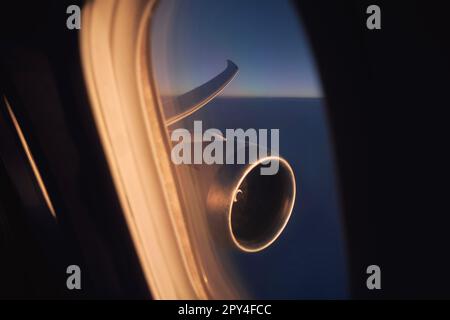 View from window of airplane during flight above clouds at dawn. Selective focus on jet engine and aircraft wing. Stock Photo
