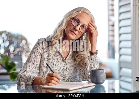 This migraine is gonna prevent me from getting anything done. an attractive senior businesswoman suffering with a headache while working from home. Stock Photo