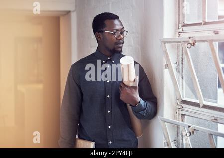 Youre looking at a top class designer. a handsome young male architect holding a scroll of blueprints while standing in a modern office. Stock Photo