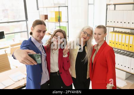Man holds smartphone taking selfie with female colleagues Stock Photo