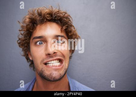 Young man, portrait and silly face for funny or goofy expression against a gray wall background. Male with crazy humor or impression looking and Stock Photo
