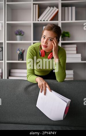 Portrait of a stressed and thoughtful millennial Asian businesswoman in casual clothes leaning on sofa with serious expression. Stock Photo
