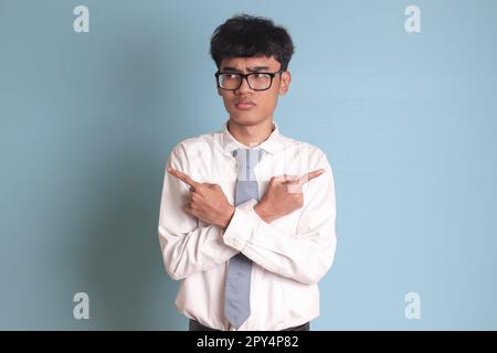 Confused senior high school student wearing white shirt uniform with gray tie with crossed hands, pointing sideways, making choice, choosing between t Stock Photo